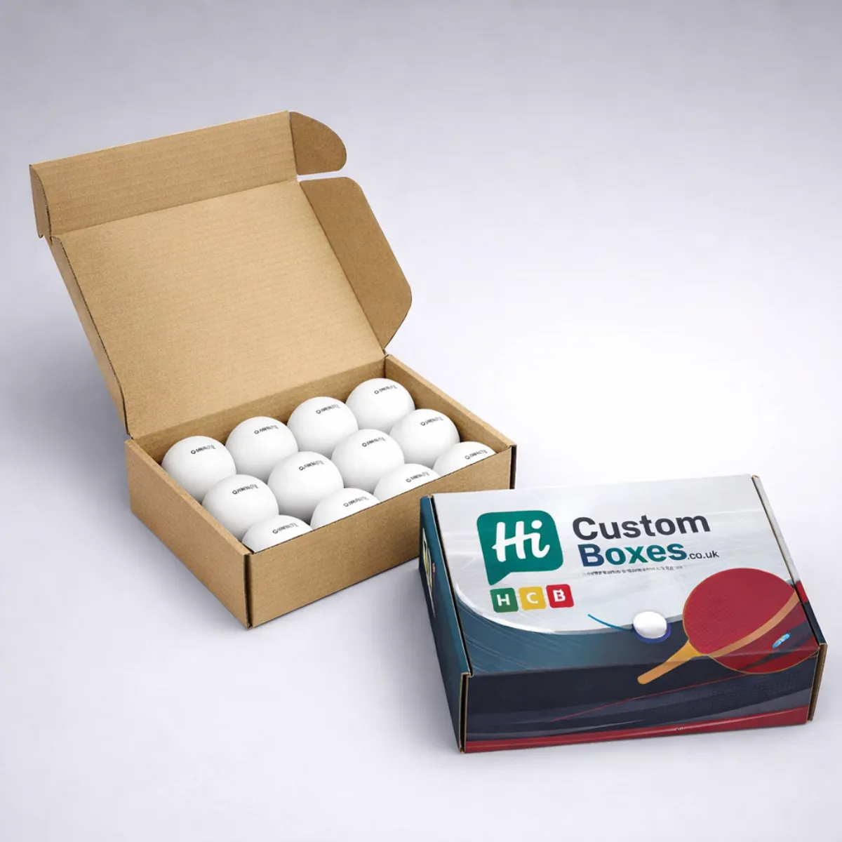 An open cardboard mailer box filled with white table tennis balls next to a branded box. class=